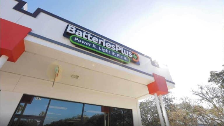 News 7 A Batteries Plus storefront with the slogan "Power it. Light it. Fix it." displayed under the store's name. The building features red accents and a glass entrance door.