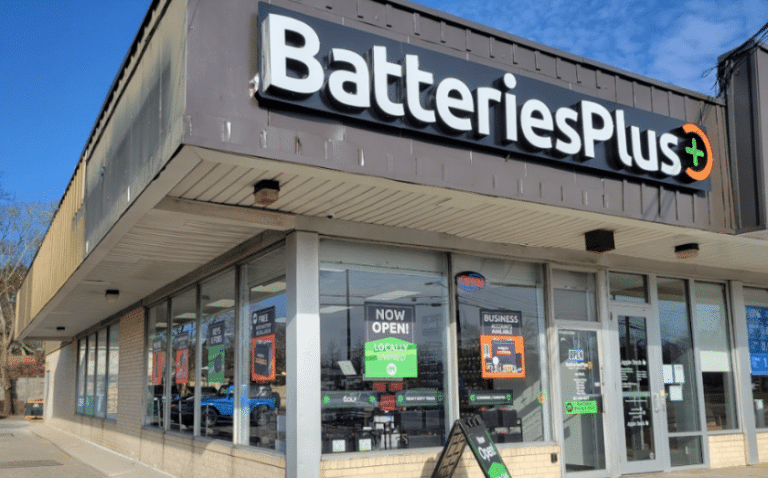 News 2 Exterior view of a Batteries Plus store in daylight, showcasing the sign and street-facing windows with various advertisements.